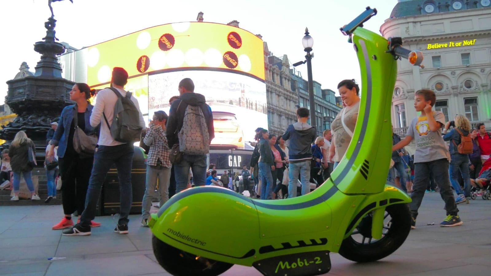 Mobi-2 na Piccadilly Circus w ciągu dnia, w tle przechodnie i ekrany reklamowe.