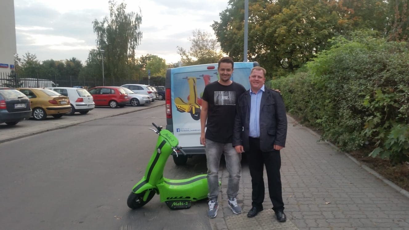 Mobi-2 na parkingu w Polsce, obok dwie osoby przy samochodzie dostawczym.