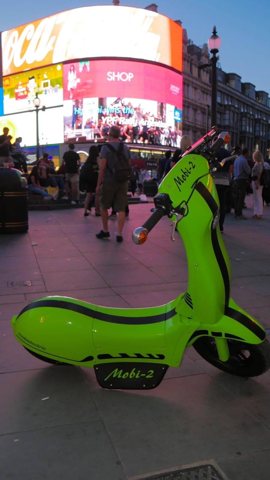 Mobi-2 z profilu na Piccadilly Circus: limonkowa karoseria, boczny podest z napisem Mobi-2, w tle rozświetlone billboardy.